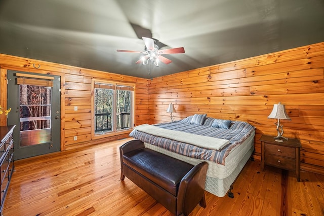 bedroom with ceiling fan, wood walls, and light wood-type flooring