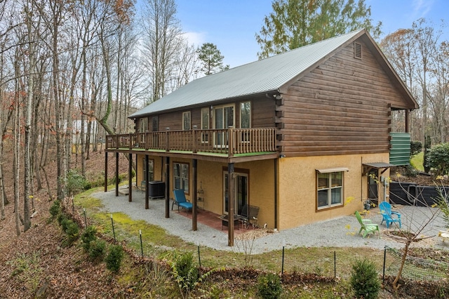 back of property with log exterior, a patio, metal roof, a wooden deck, and stucco siding