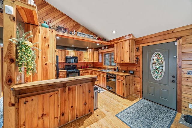 kitchen with vaulted ceiling, light countertops, light wood-type flooring, black appliances, and a sink