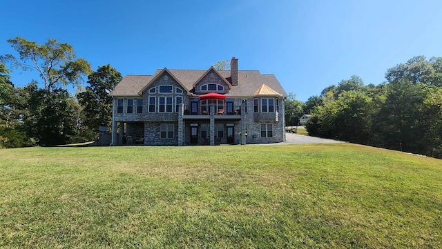 rear view of house featuring stone siding, a yard, a chimney, and a balcony