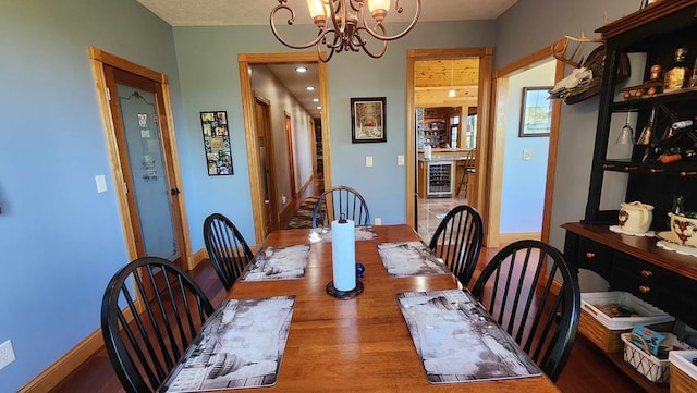 dining space featuring a chandelier, wine cooler, baseboards, and wood finished floors