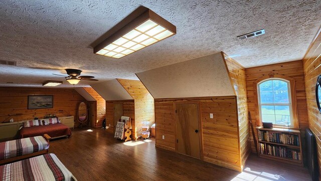 interior space with visible vents, wood finished floors, vaulted ceiling, a textured ceiling, and wood walls