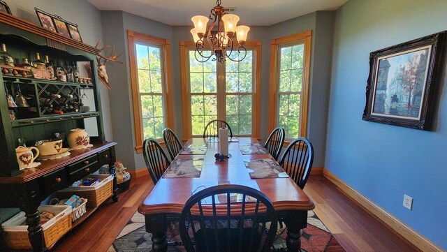 dining room with baseboards, a healthy amount of sunlight, an inviting chandelier, and wood finished floors