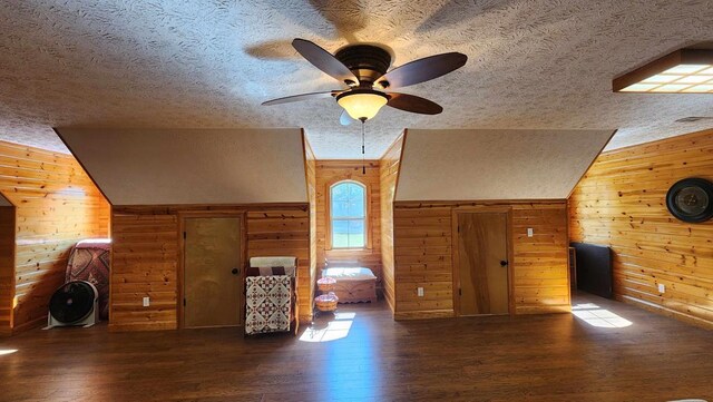 unfurnished living room featuring vaulted ceiling, dark wood-type flooring, wood walls, and a textured ceiling