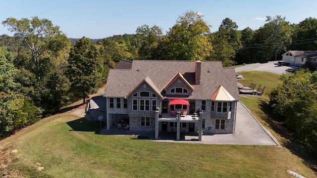 back of house featuring stone siding, a patio area, a chimney, and a yard