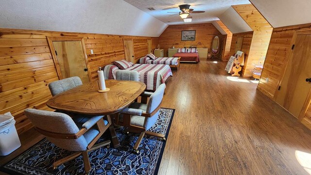 dining space with a ceiling fan, wood finished floors, vaulted ceiling, a textured ceiling, and wood walls