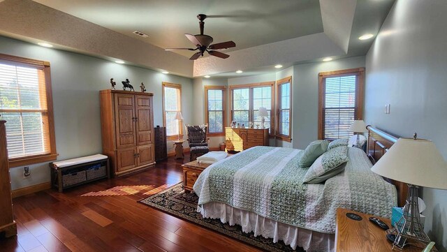 bedroom featuring dark wood-type flooring, a tray ceiling, multiple windows, and baseboards