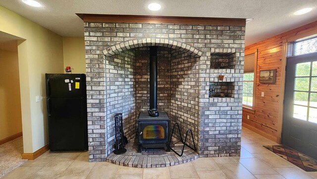 interior space featuring freestanding refrigerator, a wood stove, a textured ceiling, and baseboards