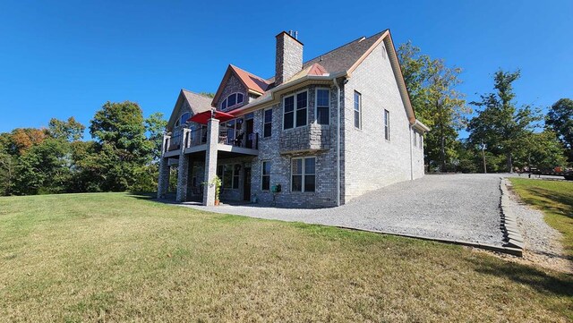 back of property featuring brick siding, a lawn, a chimney, and a balcony