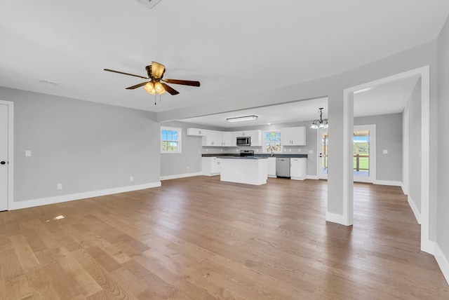 unfurnished living room featuring ceiling fan with notable chandelier, baseboards, visible vents, and light wood-style floors