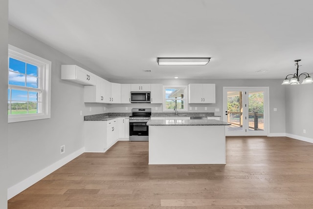 kitchen with dark stone counters, a kitchen island, appliances with stainless steel finishes, hanging light fixtures, and white cabinetry