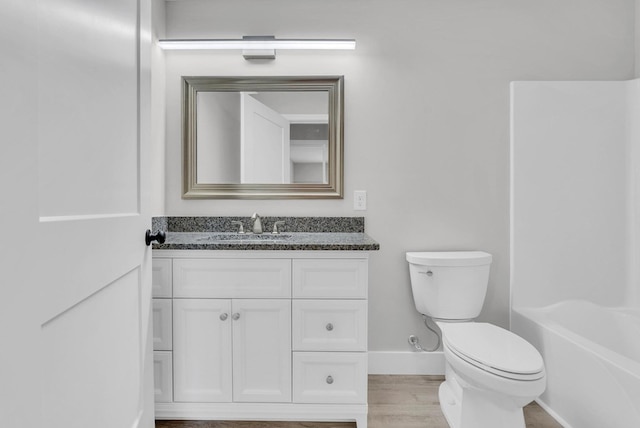 bathroom featuring toilet, washtub / shower combination, vanity, wood finished floors, and baseboards