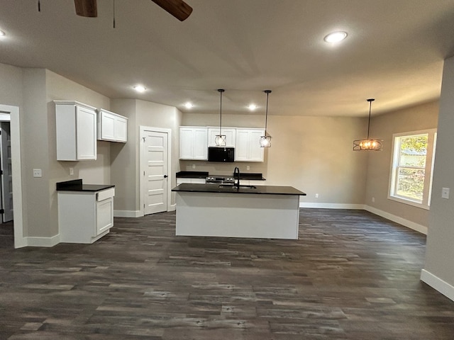 kitchen with pendant lighting, dark countertops, black microwave, and a kitchen island with sink