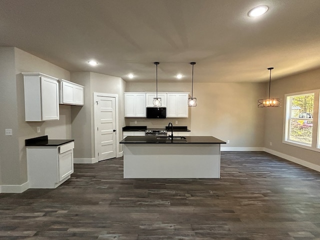 kitchen with a kitchen island with sink, black microwave, decorative light fixtures, and dark countertops