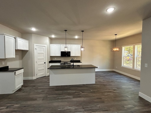 kitchen featuring dark countertops, a kitchen island with sink, black microwave, and hanging light fixtures