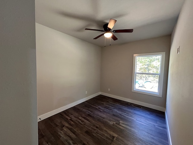 empty room featuring dark wood-type flooring, a ceiling fan, and baseboards