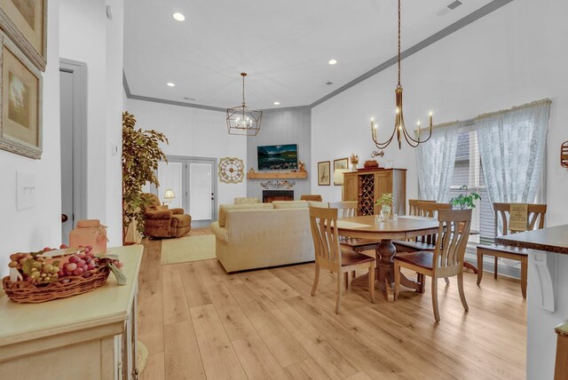 dining area with a high ceiling, crown molding, light wood-style floors, a fireplace, and a notable chandelier