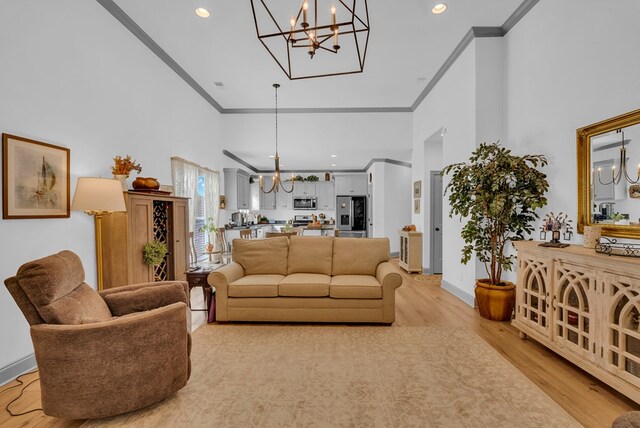 living area featuring a towering ceiling, an inviting chandelier, light wood finished floors, and crown molding