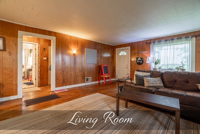 living room featuring baseboards, wooden walls, visible vents, and wood finished floors