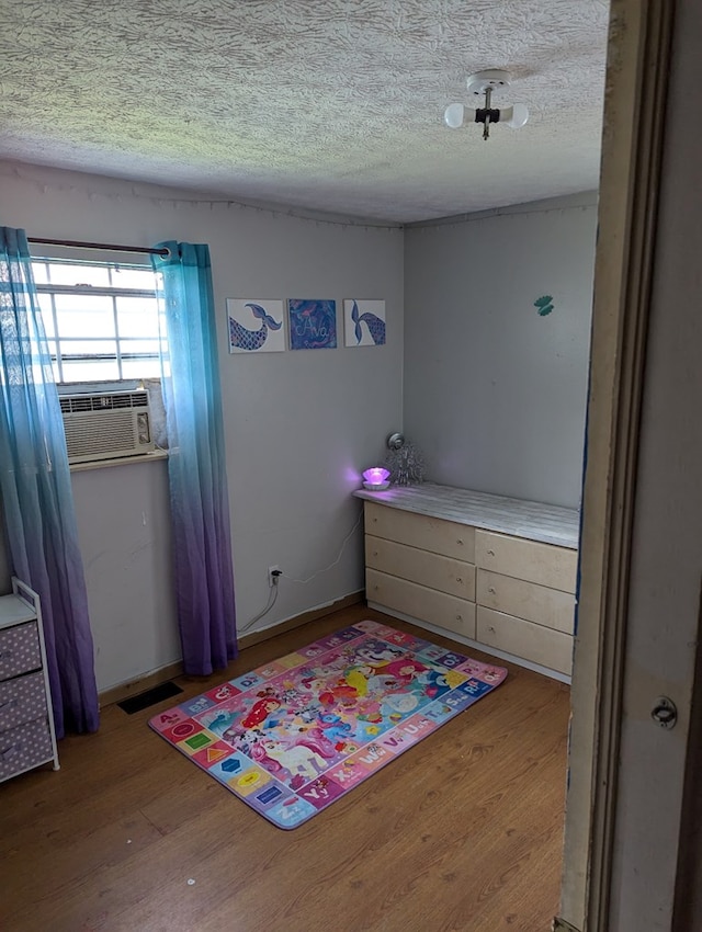 bedroom with cooling unit, visible vents, a textured ceiling, and wood finished floors