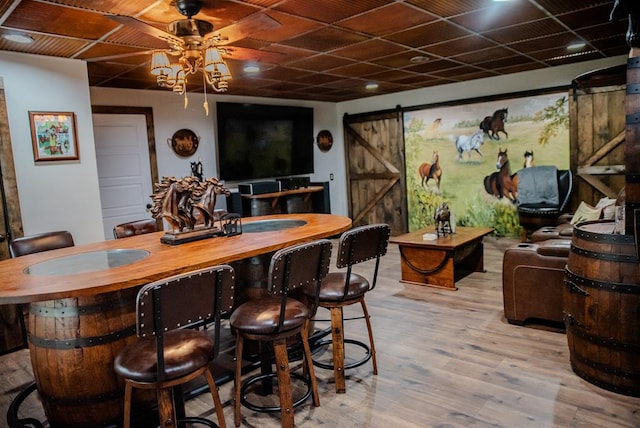 bar with ceiling fan, a barn door, light wood-type flooring, and bar