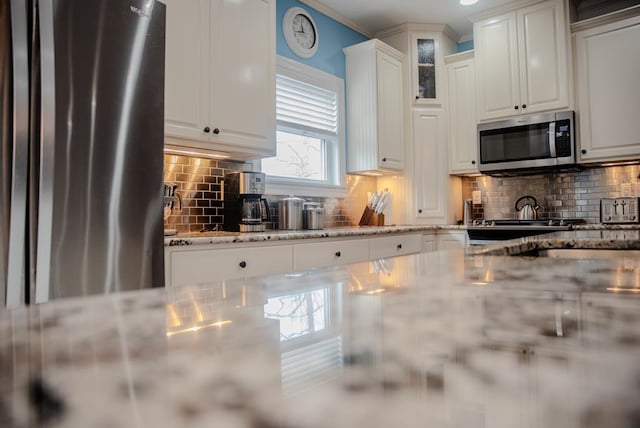 kitchen with tasteful backsplash, appliances with stainless steel finishes, glass insert cabinets, white cabinets, and light stone countertops