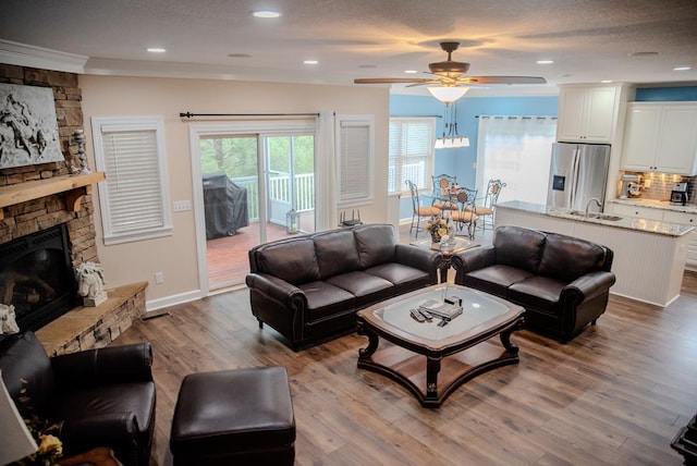 living room with ceiling fan, a stone fireplace, recessed lighting, baseboards, and light wood finished floors