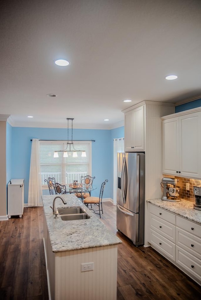 kitchen with stainless steel fridge, hanging light fixtures, a kitchen island with sink, crown molding, and a sink