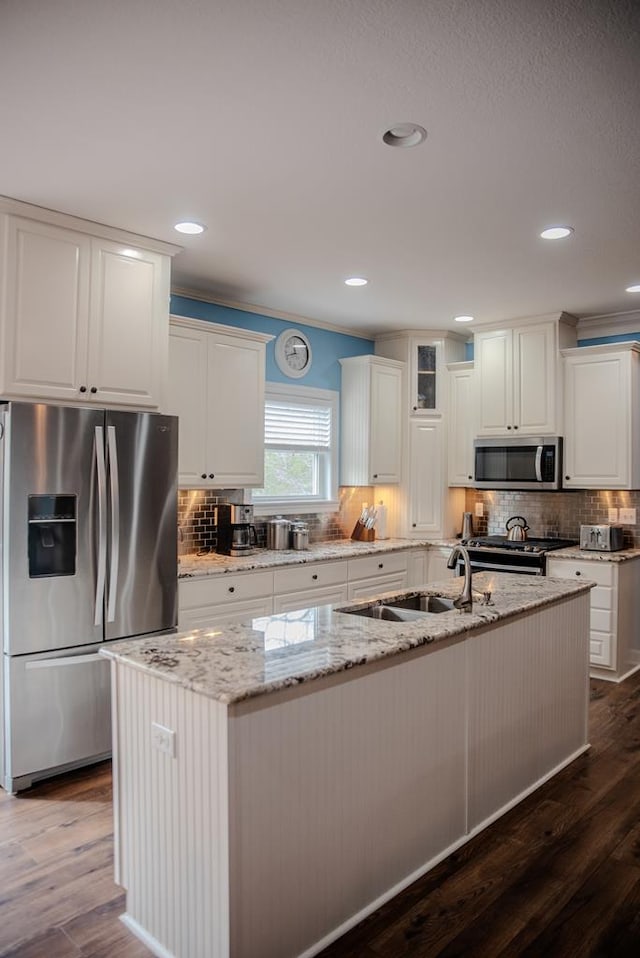 kitchen with stainless steel appliances, a kitchen island with sink, a sink, and glass insert cabinets