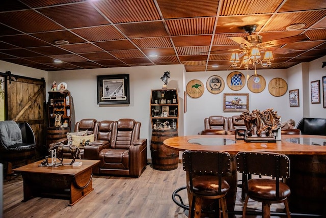 bar with a barn door, a ceiling fan, and wood finished floors