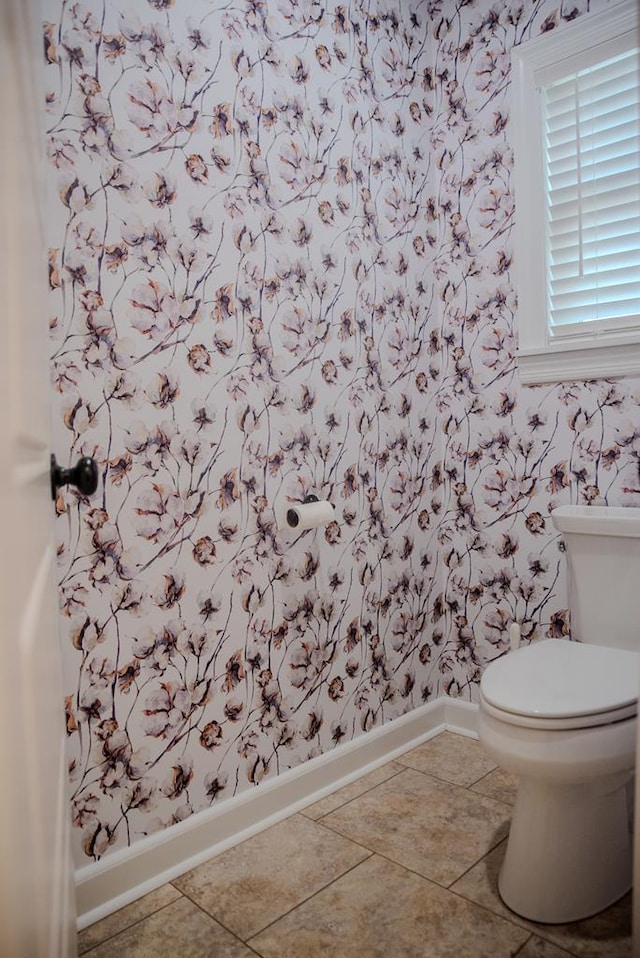 half bathroom with tile patterned flooring, baseboards, toilet, and wallpapered walls