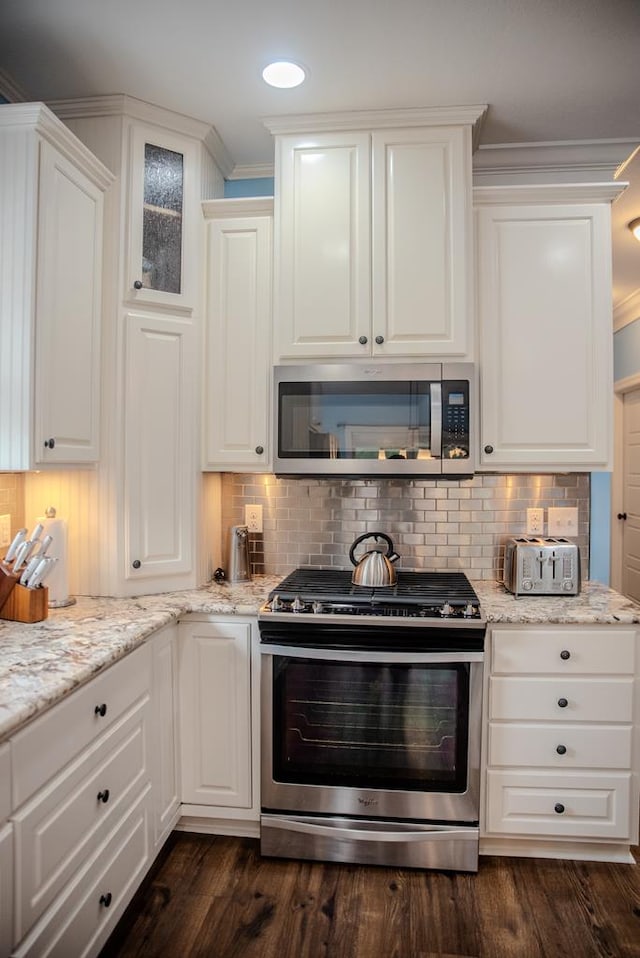 kitchen with stainless steel appliances, white cabinetry, ornamental molding, decorative backsplash, and dark wood finished floors