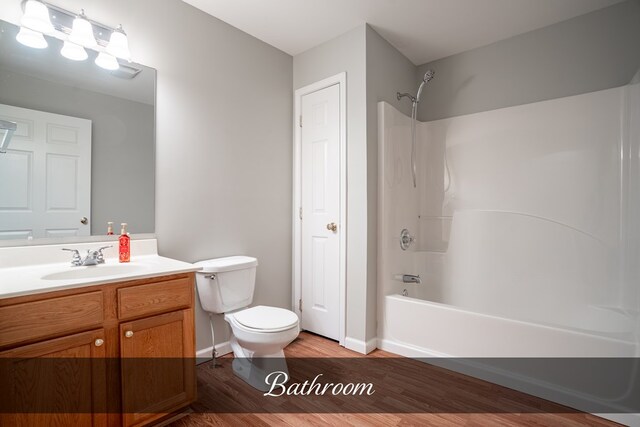 full bathroom with shower / washtub combination, toilet, vanity, wood finished floors, and baseboards