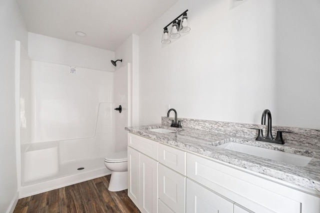 full bath with double vanity, wood finished floors, a sink, and toilet