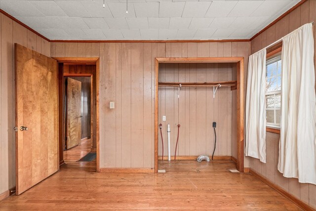 unfurnished bedroom featuring light wood finished floors, crown molding, baseboards, and a closet