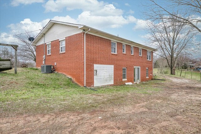 view of side of property featuring a garage, a yard, brick siding, and central AC unit