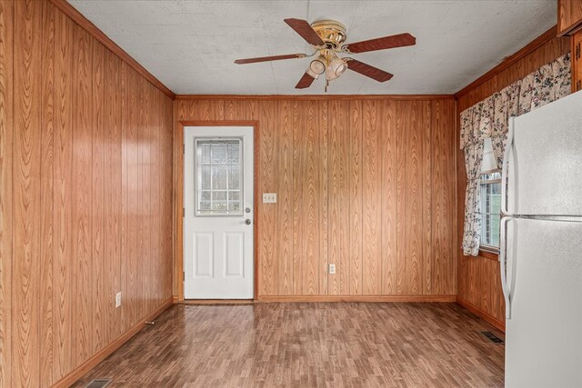 empty room featuring ceiling fan, wood walls, wood finished floors, baseboards, and crown molding