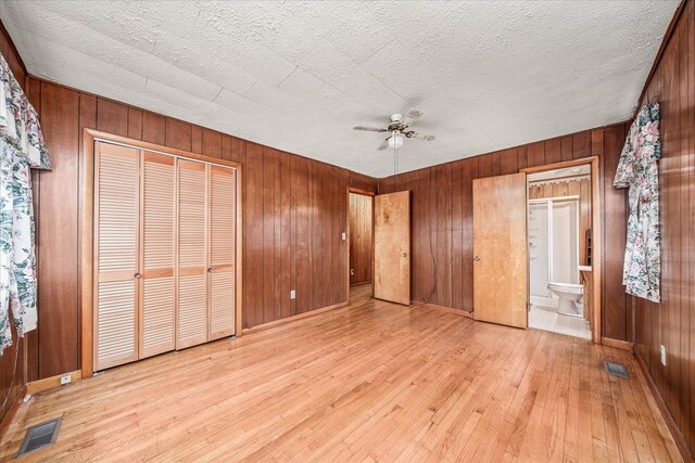 unfurnished bedroom featuring light wood-type flooring, wooden walls, visible vents, and a textured ceiling