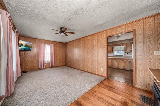 unfurnished living room with light wood-style floors, ceiling fan, wooden walls, and a textured ceiling