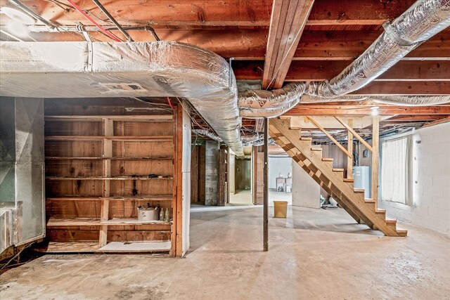 below grade area featuring water heater, stairs, and concrete block wall