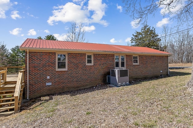 rear view of property featuring a deck, metal roof, central AC, brick siding, and a yard