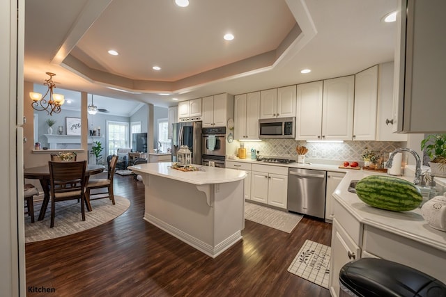 kitchen with a tray ceiling, appliances with stainless steel finishes, light countertops, and decorative light fixtures