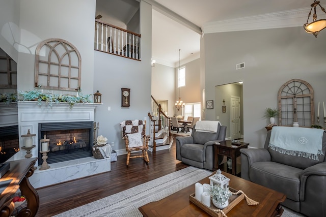 living area featuring a towering ceiling, ornamental molding, wood finished floors, a lit fireplace, and a chandelier