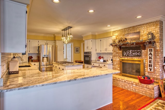 kitchen featuring stainless steel appliances, a peninsula, wood finished floors, a sink, and a brick fireplace