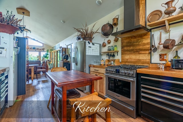 kitchen featuring stainless steel appliances, lofted ceiling, wooden counters, wood finished floors, and wall chimney exhaust hood