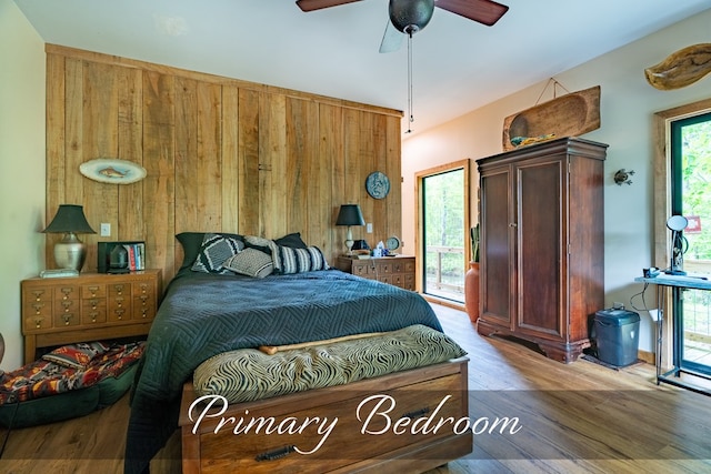 bedroom with ceiling fan, access to outside, wooden walls, and light wood-style flooring