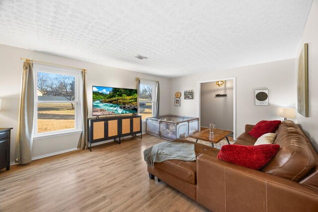 living room with light wood-type flooring, visible vents, a textured ceiling, and baseboards