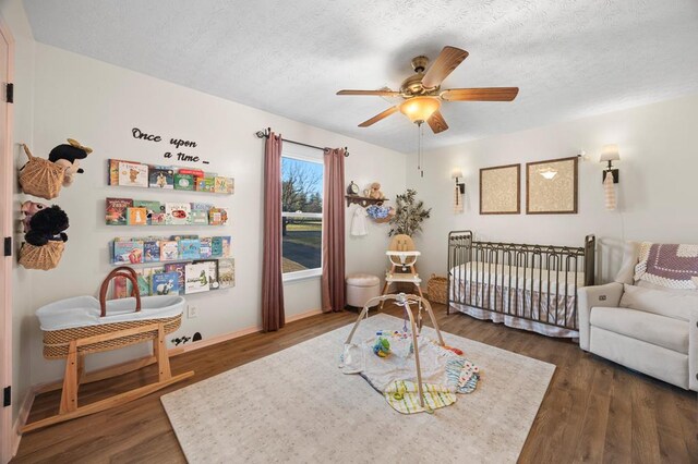 bedroom with a textured ceiling, ceiling fan, a crib, and dark wood-style flooring