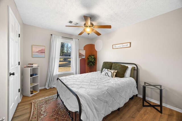 bedroom featuring baseboards, a textured ceiling, visible vents, and wood finished floors