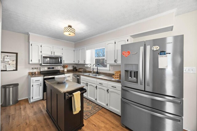 kitchen featuring dark wood-style flooring, stainless steel appliances, dark countertops, white cabinetry, and a sink